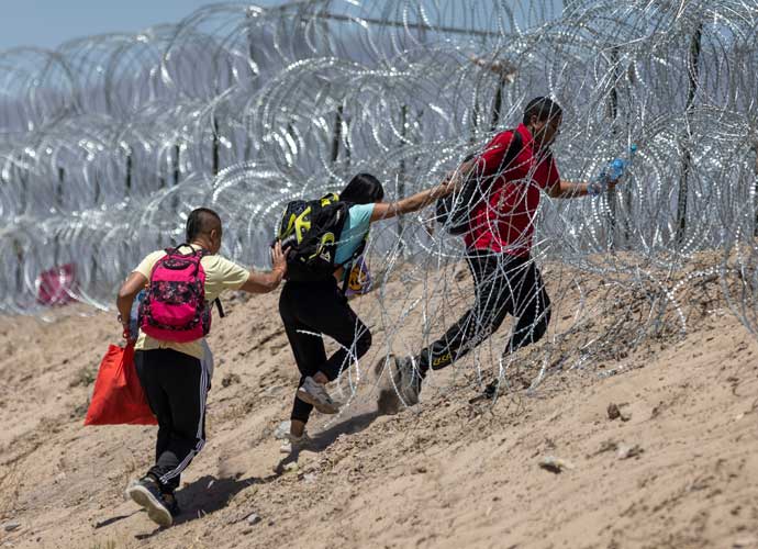 EL PASO, TEXAS - MAY 11: Immigrants walk through razor wire surrounding a makeshift migrant camp after crossing the border from Mexico on May 11, 2023 in El Paso, Texas. The number of immigrants reaching the border has surged with the end of the U.S. government's Covid-era Title 42 policy, which for the past three years has allowed for the quick expulsion of irregular migrants entering the country. (Photo by John Moore/Getty Images)